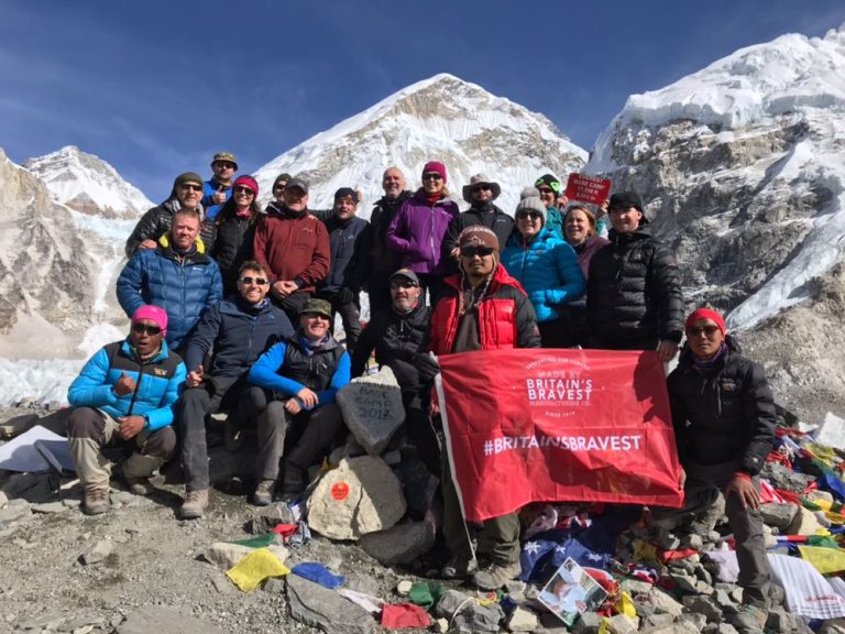 A group of veterans poses with a red flag labeled "Britain's Bravest" in a mountainous, snowy landscape, celebrating their successful resettlement from Civvy Street to the wild.