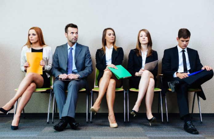 Five people in formal attire sit in chairs, holding folders, appearing to wait. Among them, a veteran is ready to transition back into Civvy Street, eager to embrace new opportunities after resettlement.