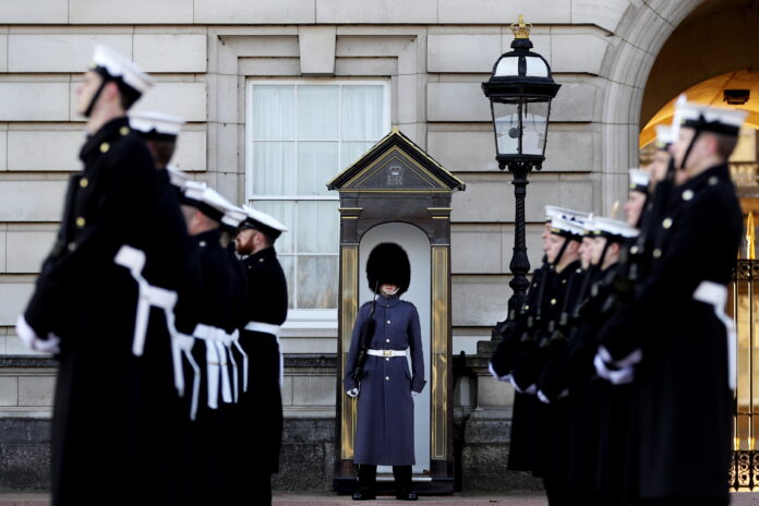 A veteran guard stands at attention under a sentry box, surrounded by a line of uniformed soldiers in a formal setting, reflecting on his journey from civvy street to this disciplined life.