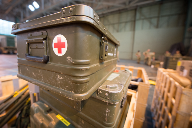 Stacked military medical supply boxes with red cross symbols are neatly arranged in a warehouse environment, ready to support resettlement efforts for veterans.