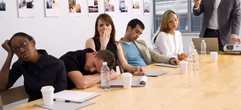A group of people appear bored and tired in a meeting room, some yawning and some resting on the table, surrounded by paper cups, water bottles, and documents—a snapshot of civilian life that sharply contrasts with the discipline of military routine.