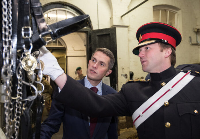 A veteran in a military uniform shows another man a piece of horse tack in a stable, sharing stories of resettlement into civvy street.