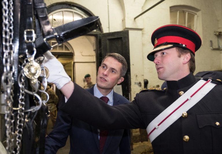A veteran in a military uniform shows another man a piece of horse tack in a stable, sharing stories of resettlement into civvy street.