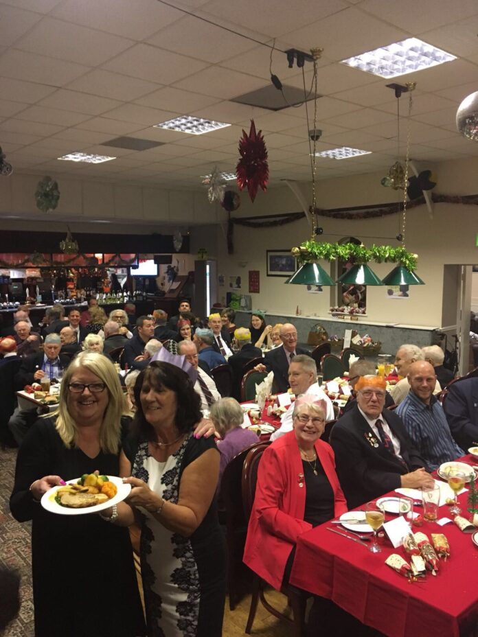 A group of people seated at tables enjoys a festive meal in a decorated room, celebrating the resettlement journey from civvy street, with two women in the foreground holding a plate of food.