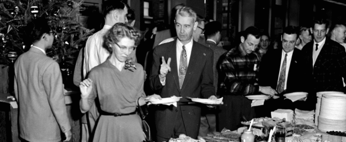 A group of people, including veterans adjusting to civvy street, gather around a table, serving themselves food at a buffet-style event. A decorated Christmas tree stands joyfully in the background.