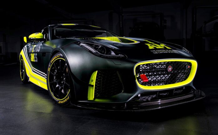 A black sports car with yellow accents and a visible Jaguar logo, showcasing racing modifications and sponsor decals, rests like a veteran from Civvy Street, parked in a dimly lit garage.