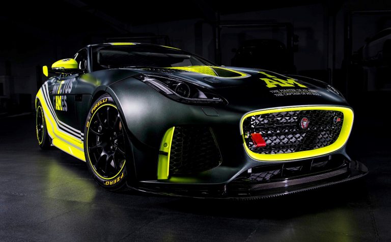A black sports car with yellow accents and a visible Jaguar logo, showcasing racing modifications and sponsor decals, rests like a veteran from Civvy Street, parked in a dimly lit garage.