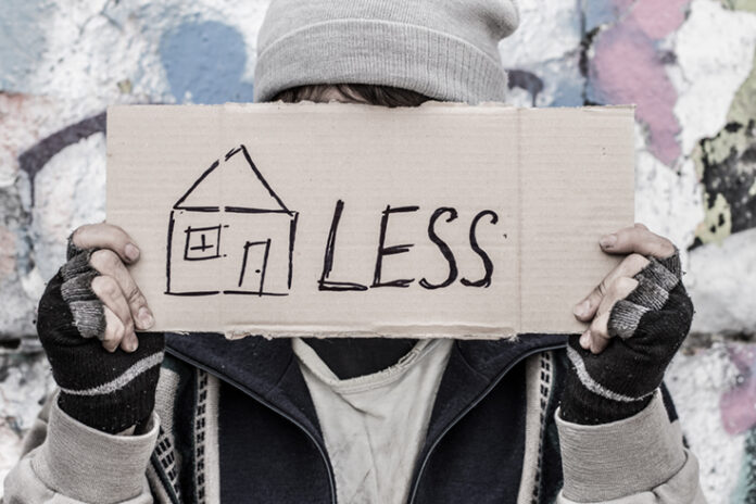 A person holds a cardboard sign with a drawing of a house and the word 