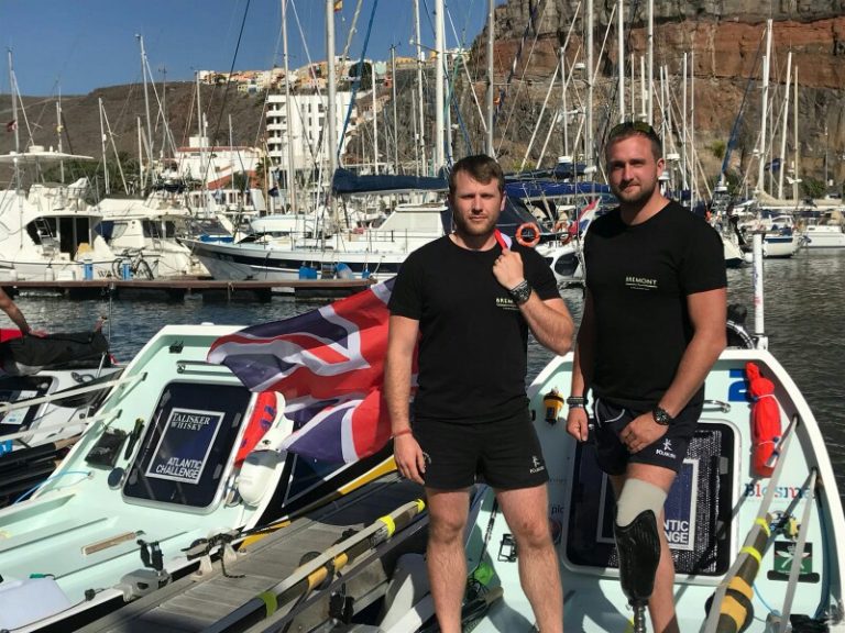 Two men in black shirts stand on a small boat adorned with the British flag, docked at a marina and surrounded by other boats. Their camaraderie speaks volumes, perhaps hinting at a shared journey from veteran duty to Civvy Street.