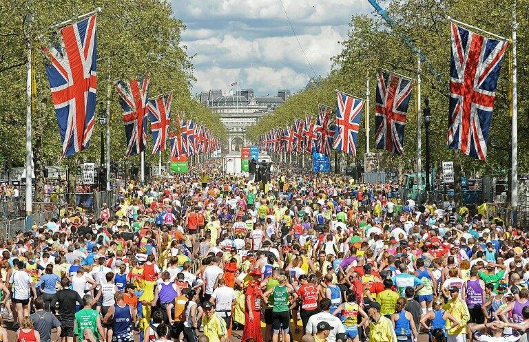A large crowd of marathon runners on a wide street lined with Union Jack flags, surrounded by spectators and trees, mirrors the journey from military life to civvy street, where resettlement becomes a new race for many veterans.