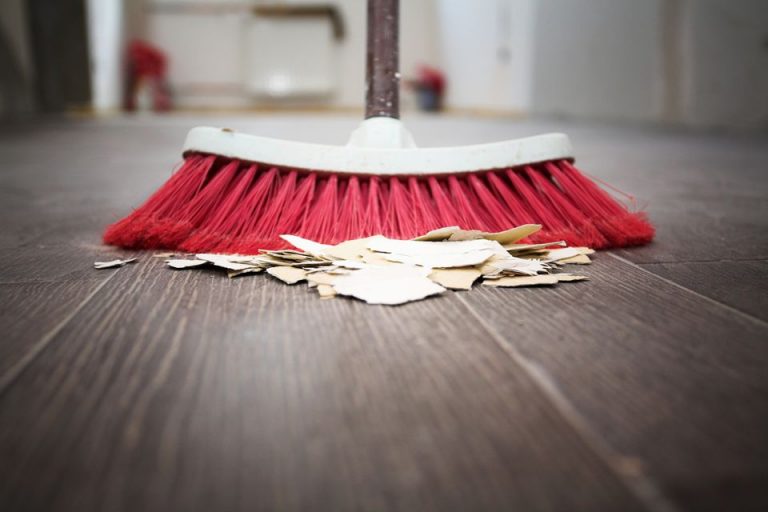 A red broom efficiently sweeps a pile of torn paper pieces on a wooden floor, much like a veteran preparing for life on Civvy Street.