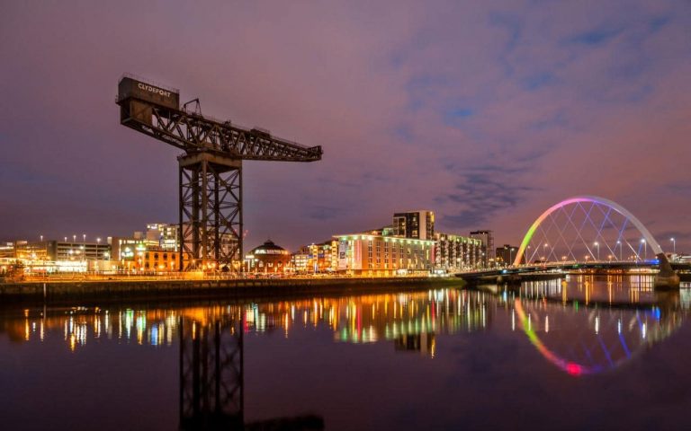 Night view of a waterfront cityscape with an illuminated arched bridge and large crane reflected in the calm water, capturing the serene transition to civvy street as veterans find new beginnings.