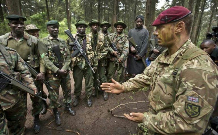 A veteran in camouflage with face paint gestures while talking to a group of uniformed soldiers in a forest, sharing insights from his transition journey from the military to civvy street.