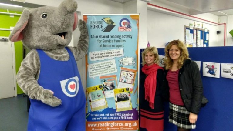 Two women stand beside a person in an elephant costume in front of a colorful banner promoting Reading Force, a reading activity designed to support service families and veterans transitioning to Civvy Street.