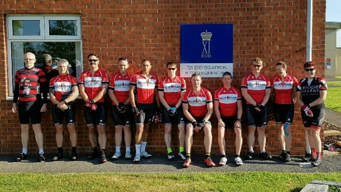 A group of cyclists in red and white jerseys, including a veteran adjusting to civvy street, stand in a line outside a brick building with a blue sign.