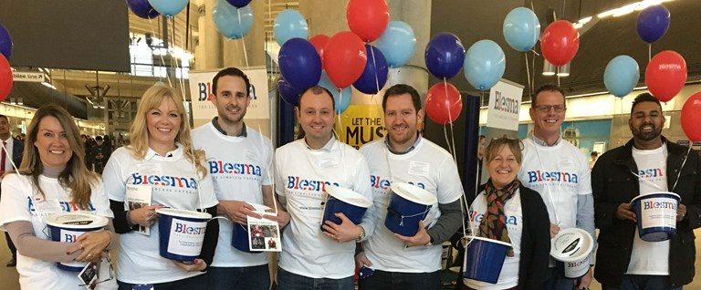 A group of veterans in Blesma shirts, embracing their resettlement journey from Civvy Street, hold donation buckets indoors, surrounded by red, blue, and light blue balloons.