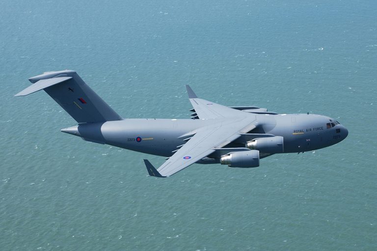 A military cargo aircraft, a testament to the veteran's journey from battlegrounds to Civvy Street, flies over a tranquil body of water.