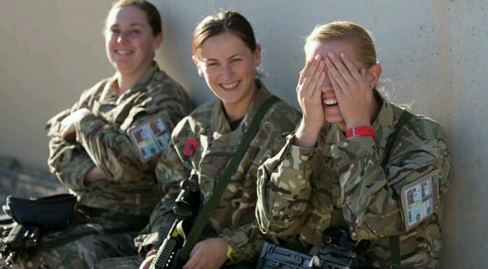 Three uniformed individuals sit against a wall. Two smile at the camera, while the third covers her face with her hands, appearing to laugh. As they share a light-hearted moment, their thoughts perhaps linger on civvy street and the resettlement process awaiting them.