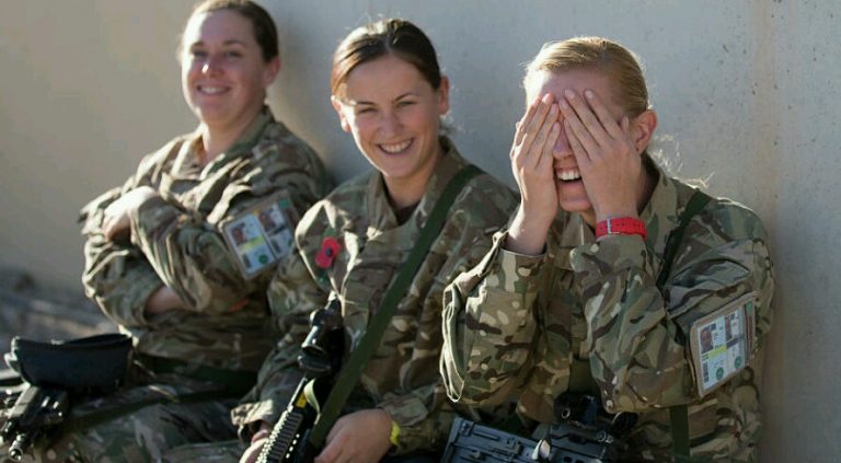 Three uniformed individuals sit against a wall. Two smile at the camera, while the third covers her face with her hands, appearing to laugh. As they share a light-hearted moment, their thoughts perhaps linger on civvy street and the resettlement process awaiting them.