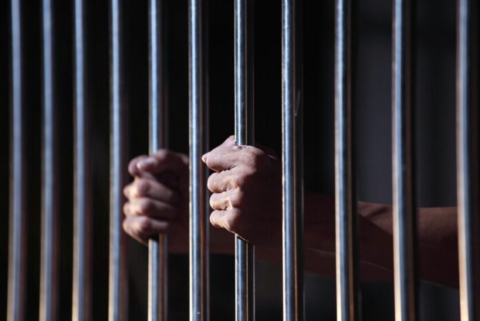 Hands gripping prison cell bars tightly in dim lighting, the veteran yearns for resettlement to Civvy Street.