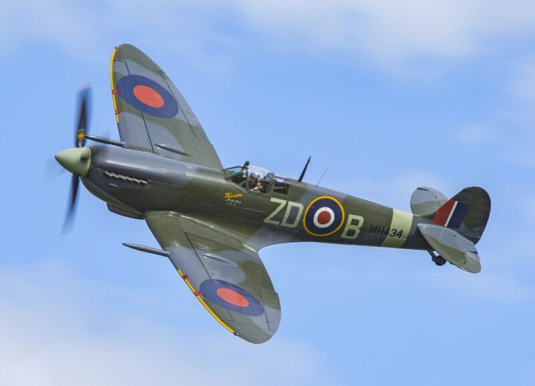 A vintage military aircraft, a Spitfire, flies against a blue sky, echoing the tales of a veteran transitioning to civvy street. The plane is green with RAF roundels on its wings and fuselage.