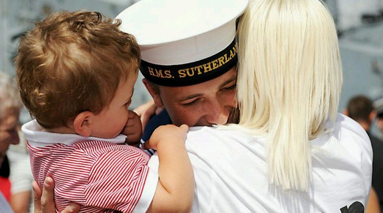 A veteran in a white uniform embraces a woman and a child wearing a red-striped shirt, savoring the joys of Civvy Street.