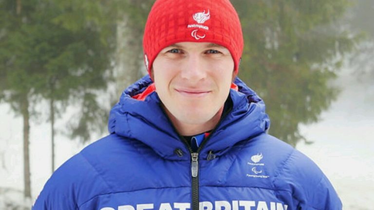 A veteran wearing a red hat and blue jacket emblazoned with "Great Britain" stands outdoors in a snowy forest setting, reflecting on their resettlement journey from civvy street.
