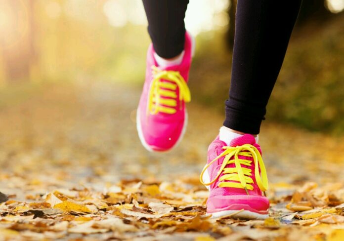 Close-up of a veteran running on a leaf-covered path, wearing bright pink and yellow athletic shoes, embracing the spirit of resettlement with each stride.