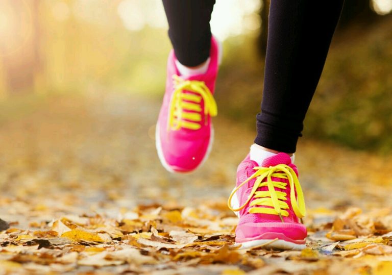 Close-up of a veteran running on a leaf-covered path, wearing bright pink and yellow athletic shoes, embracing the spirit of resettlement with each stride.