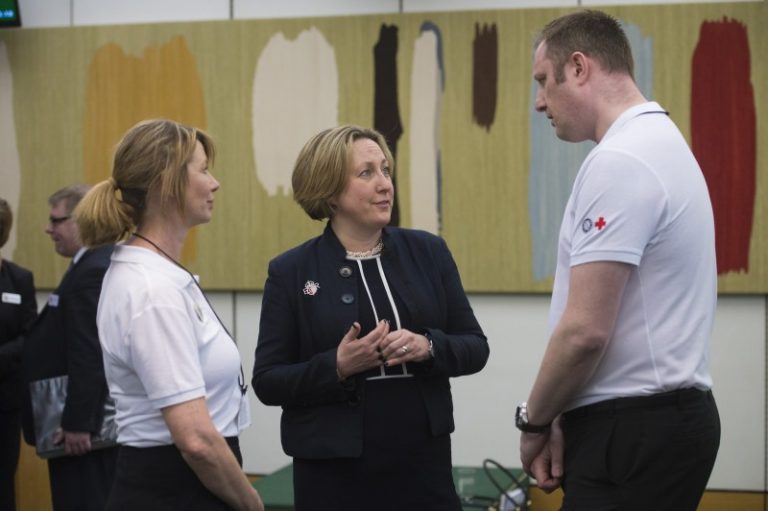 Three people engaged in conversation in an indoor setting, with two wearing white shirts featuring logos and the third clad in business attire. The topic seems to revolve around resettlement into civvy street. Abstract art decorates the wall in the background, adding a touch of creativity to their discussion.