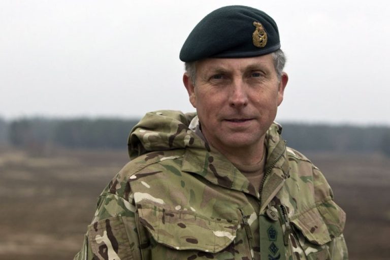 A veteran in military camouflage uniform and beret stands outdoors, ready to transition to Civvy Street, with a blurred landscape in the background.