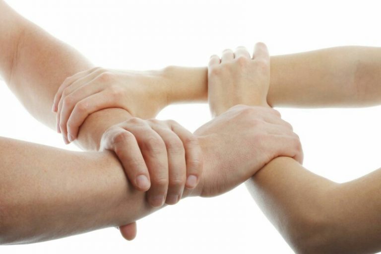 Four hands, symbolizing resettlement, grasp each other's wrists in a linked circle against a white background.