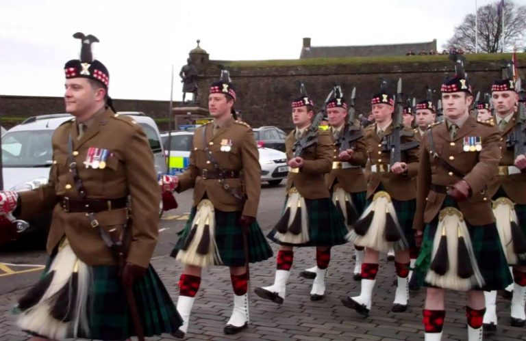 A group of veterans in military uniforms with kilts and feathered hats march in formation on a street, proudly showcasing their transition from service to civvy street.