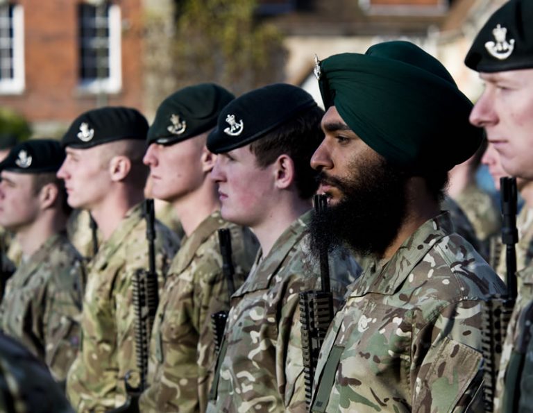 A row of soldiers in camouflage uniforms and green berets stand at attention. One soldier, a veteran embracing life after resettlement, wears a green turban.