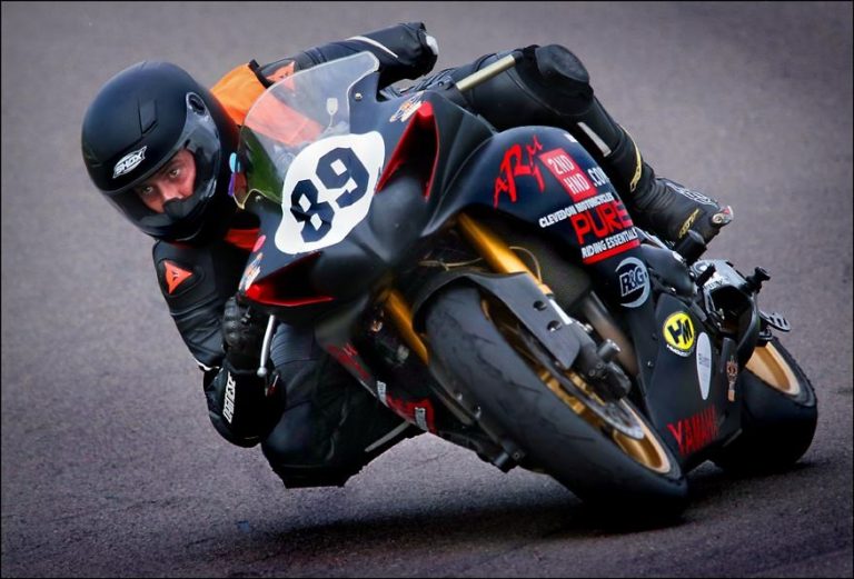 A veteran motorcyclist leans into a curve on the track, wearing a helmet while riding a black and red motorcycle with number 89, reminiscent of his resettlement from Civvy Street to racing adrenaline.