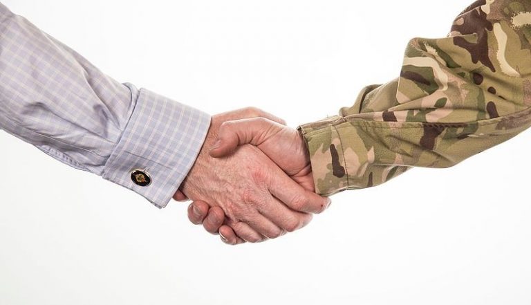 A person in a plaid shirt shakes hands with a veteran in a camouflage uniform, symbolizing cooperation and resettlement into Civvy Street.