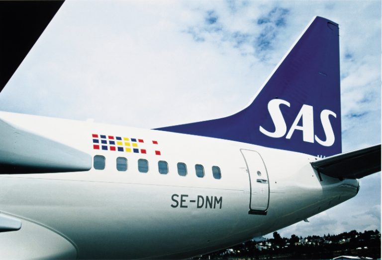 Close-up of a Scandinavian Airlines (SAS) airplane tail marked with registration SE-DNM, featuring a blue and white logo and flag emblems, reminiscent of a pathfinder leading the way through the skies.