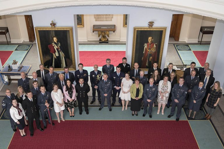 Group photo of veterans in formal attire standing in a grand room with two large portraits on the walls, celebrating their resettlement into Civvy Street.
