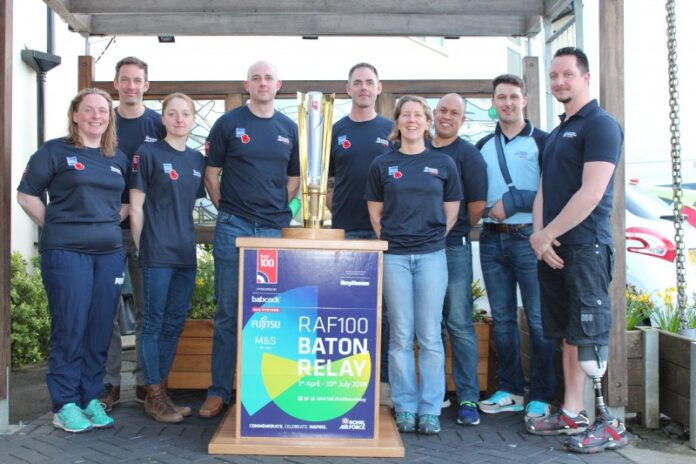 A group of people in matching shirts, including a proud Army veteran, stand around a large trophy labeled 