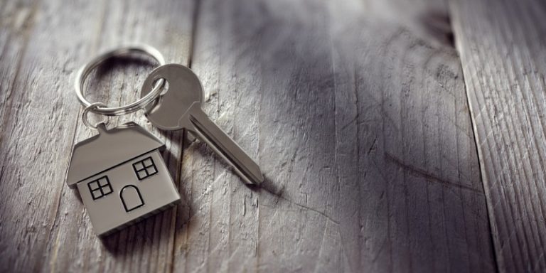 A key with a house-shaped keychain rests on a wooden surface, ready for its new mission in resettlement—its next adventure akin to that of an Army veteran transitioning from service to civilian life.