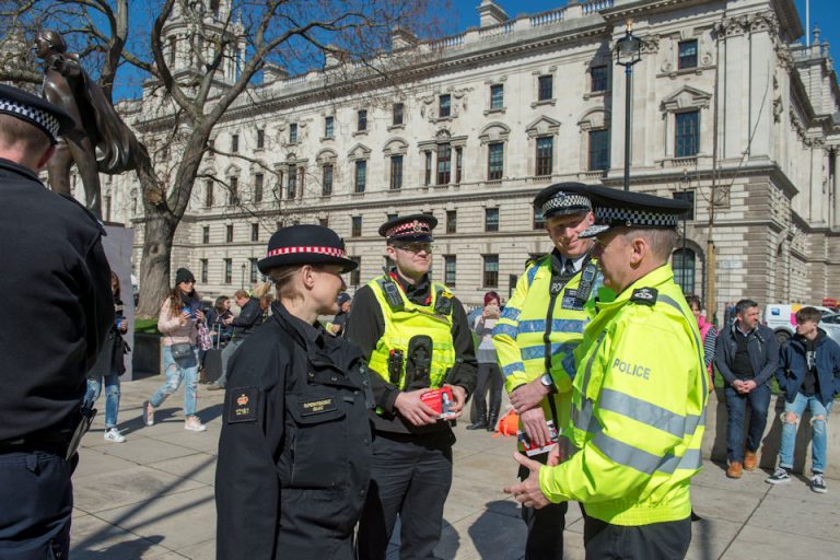 Police officers in uniform converse outside a historic building as people walk by in the background, reminiscent of veterans adjusting to civvy street after resettlement.