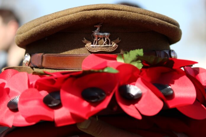 A Royal Navy military cap adorned with a badge, surrounded by bright red poppies.