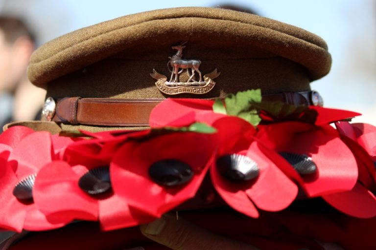 A Royal Navy military cap adorned with a badge, surrounded by bright red poppies.