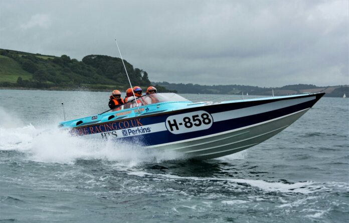 A veteran navigates the speedboat labeled H-858 as it races through the water, with three helmeted passengers onboard.