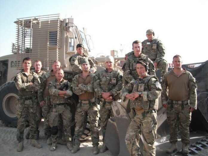 A group of veterans in uniform pose proudly in front of a military vehicle amidst the desert landscape, reminiscing about their journey from combat zones to civvy street.