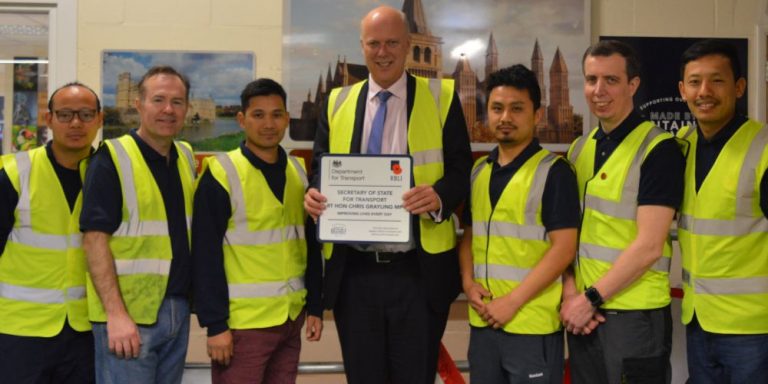 A group of seven people in high-visibility vests stands together, celebrating a resettlement success. One individual proudly holds a framed certificate, marking their transition to Civvy Street.