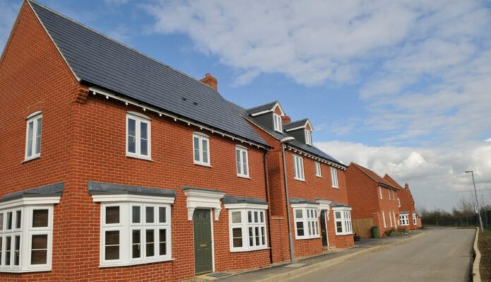 Red brick row houses with white windows and gray roofs line a quiet street, offering a peaceful resettlement haven for veterans under a partly cloudy sky.