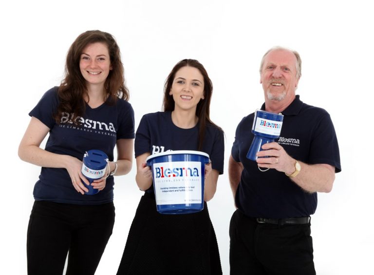 Three people wearing Blesma shirts, representative of the veteran resettlement community, hold donation containers and smile at the camera on a white background.