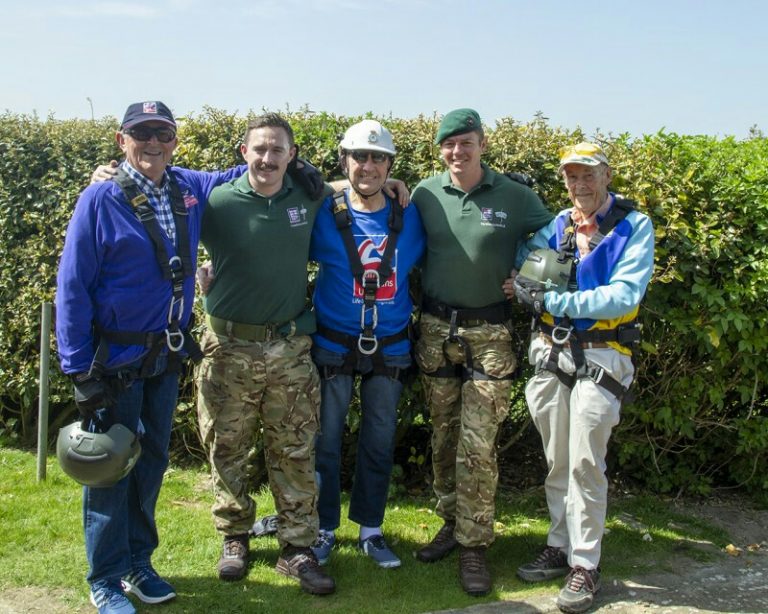 Five people standing outdoors, wearing harnesses, with two in camouflage pants and three in blue jackets, all smiling like a cheery Army Pathfinder team.