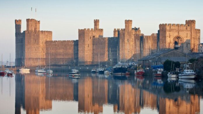 A large stone castle with multiple towers is reflected in a calm body of water, as if standing sentinel for the pathfinder boats moored in the foreground.